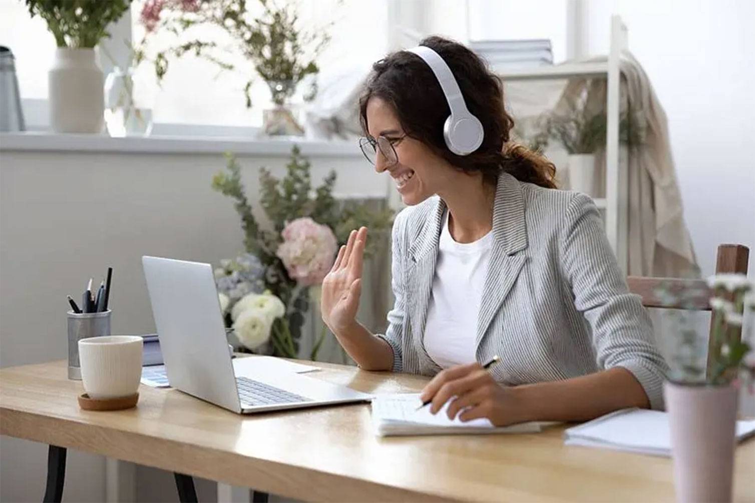Office worker with headphones waving at the laptop screen.